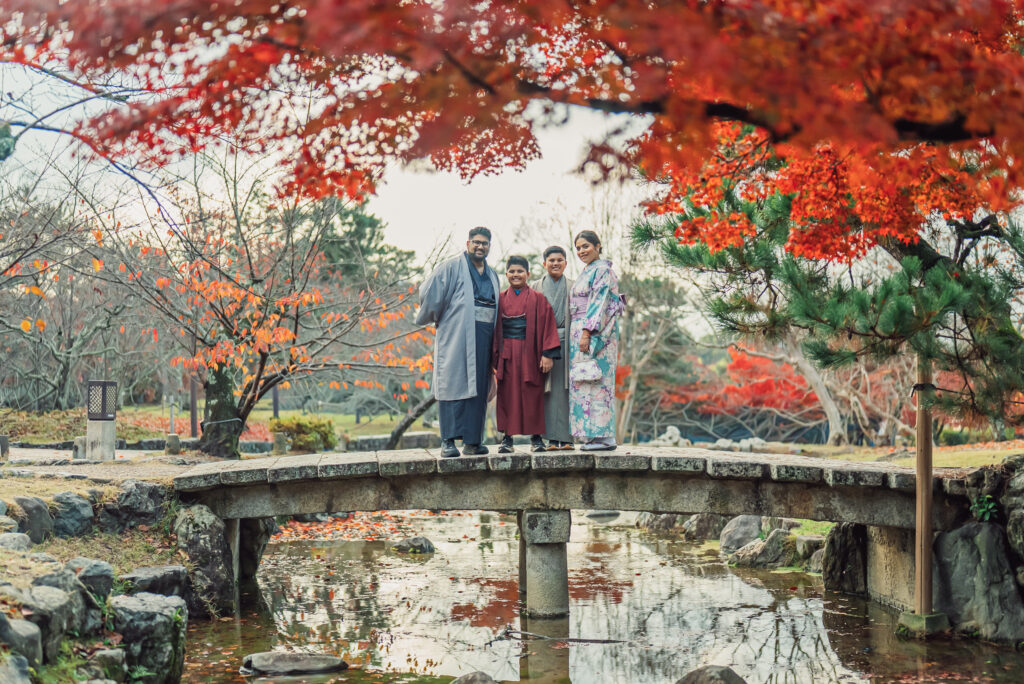 A family wearing kimono smiling together on a bridge surrounded by beautiful autumn leaves at Maruyama Park Kyoto