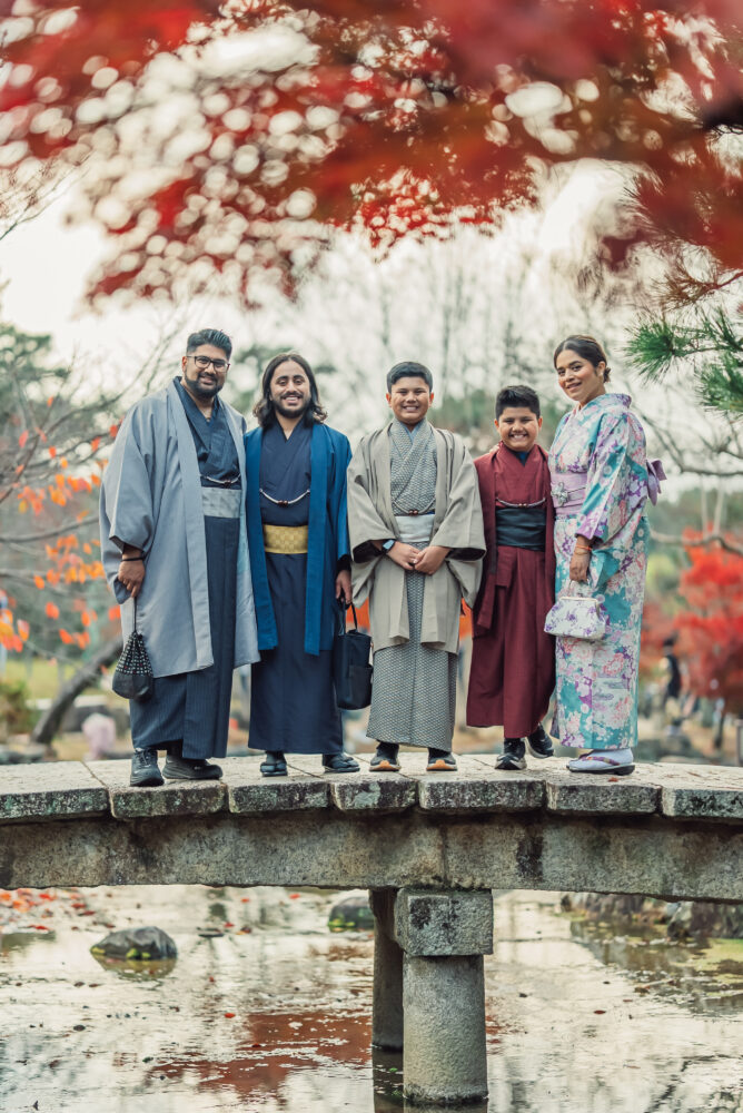 A family taking a photo in traditional kimono on a bridge with colorful autumn foliage at Maruyama Park in Kyoto