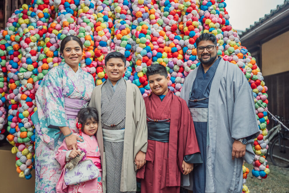 A family taking photos in front of colorful kukurizaru at Yasaka Koshindo Temple during a Kyoto family photoshoot