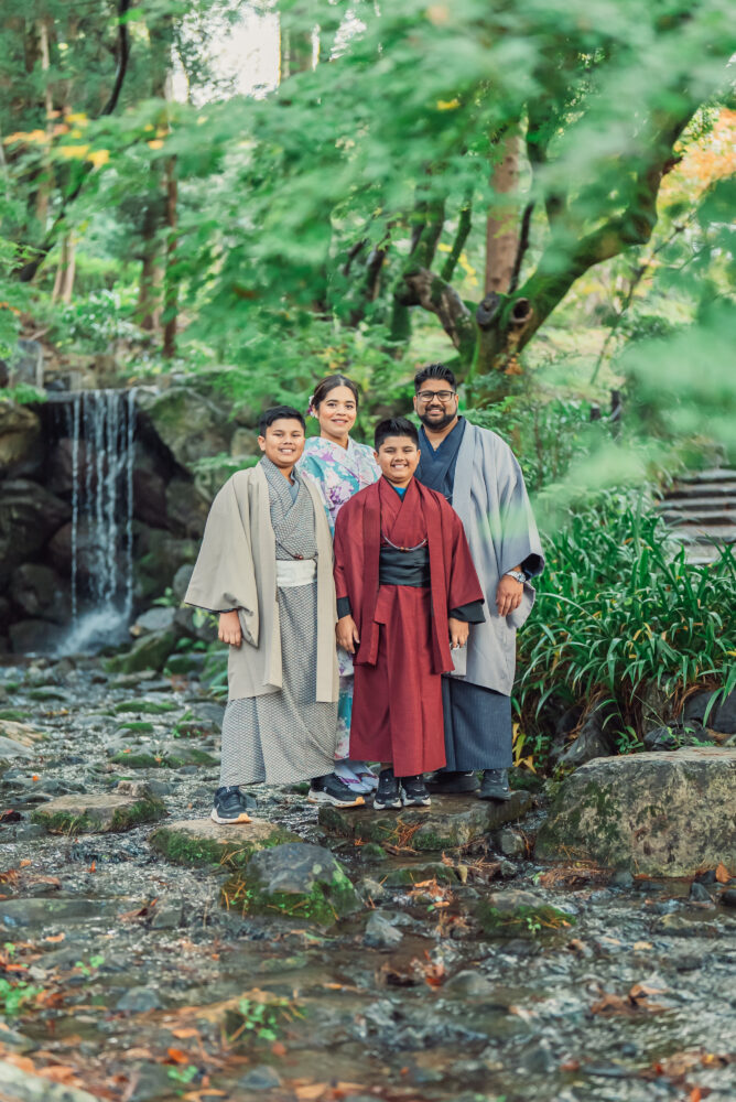 A family standing on stepping stones in front of a waterfall during a Kyoto family photoshoot at Maruyama Park