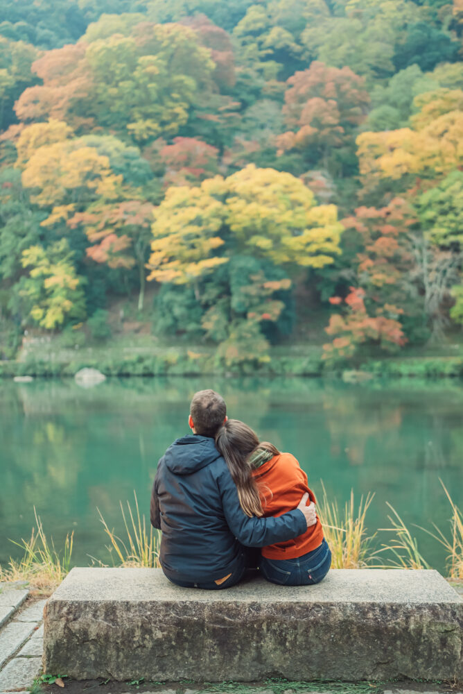 Cinematic engagement portrait of a couple standing beneath colorful autumn leaves in Kyoto
