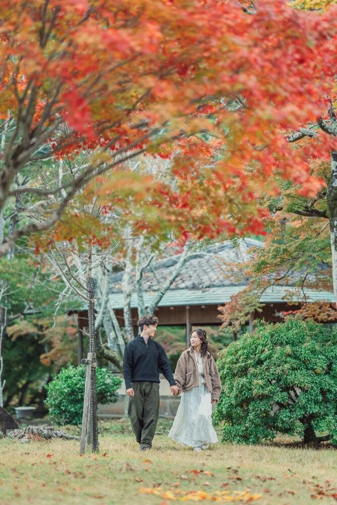 Romantic engaged couple standing beneath colorful autumn foliage in Arashiyama Kyoto