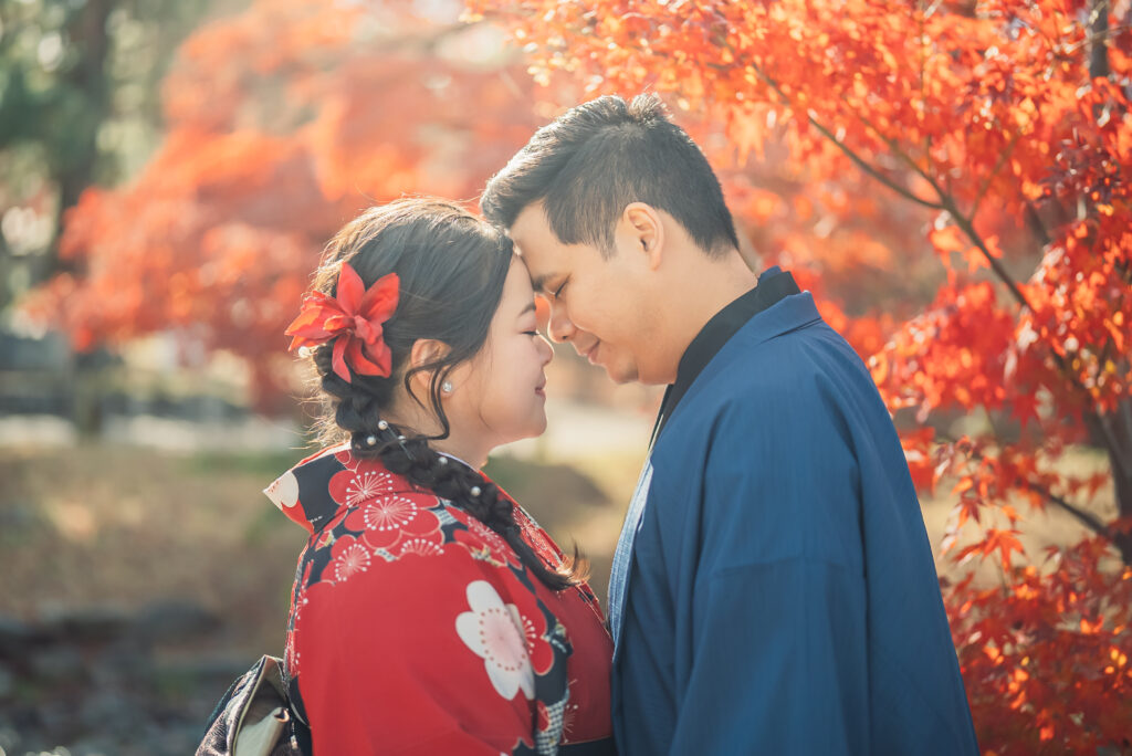 A couple touching foreheads together in front of beautiful red autumn leaves during a Kyoto kimono couple photoshoot at Maruyama Park