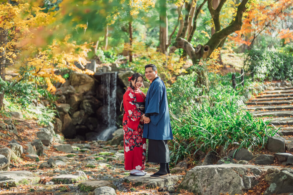 A couple standing on stepping stones in front of a waterfall during a romantic Kyoto couple photoshoot