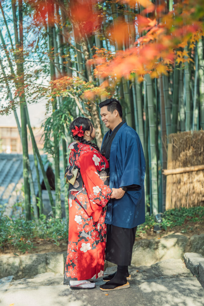 A couple posing together surrounded by the beautiful contrast of bamboo forest and autumn leaves during a Kyoto photoshoot
