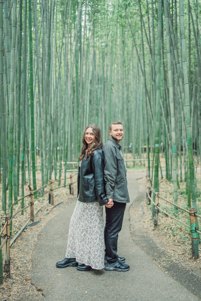 A couple standing back to back surrounded by bamboo trees in Arashiyama Bamboo Forest Kyoto during a romantic photoshoot