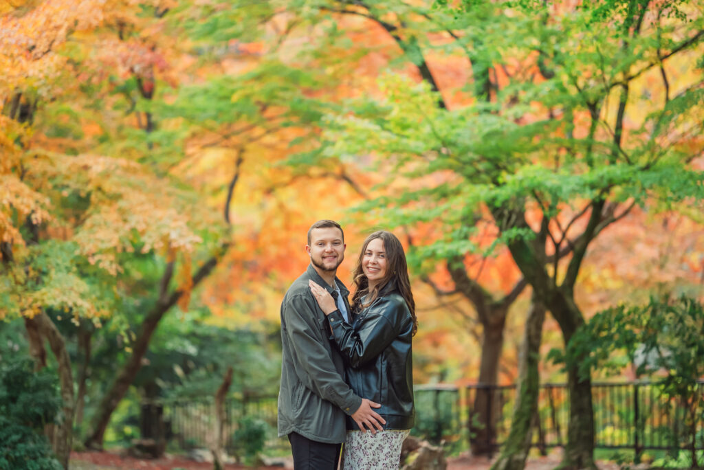 A romantic couple smiling together surrounded by beautiful autumn leaves in Arashiyama Kyoto during a fall photoshoot
