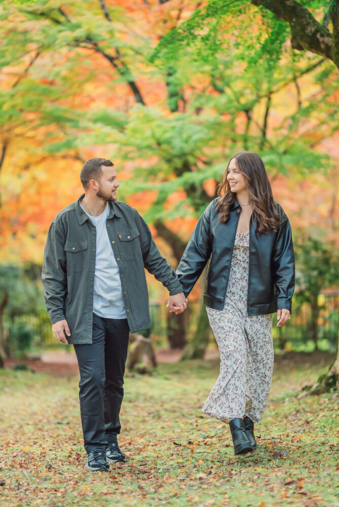 A couple walking through colorful autumn leaves in Arashiyama Kyoto during a romantic fall photoshoot