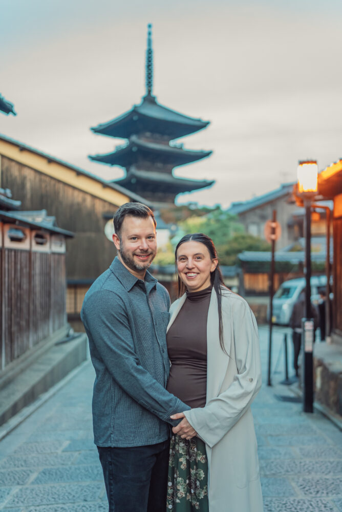 A smiling expectant couple in the soft morning light with Yasaka Pagoda in the background during a Kyoto maternity photoshoot