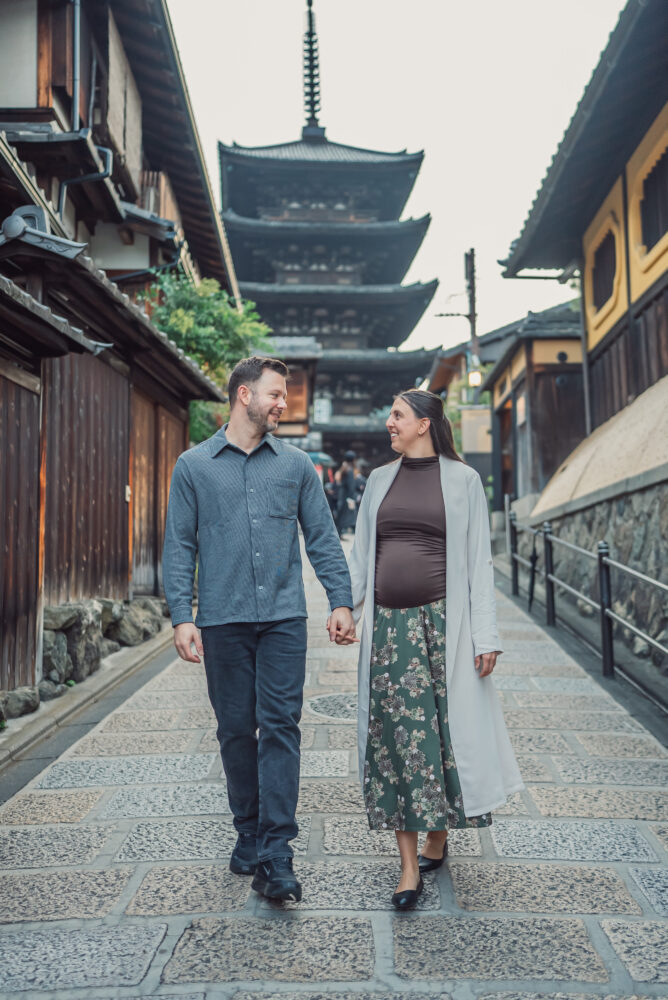 Pregnant couple holding hands and walking in front of Yasaka Pagoda during an early morning Kyoto photo session