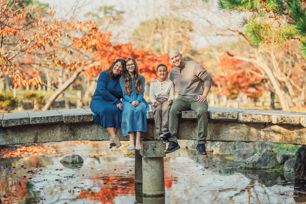 A family wearing traditional kimono sitting together on a bridge surrounded by beautiful autumn leaves in Maruyama Park Kyoto