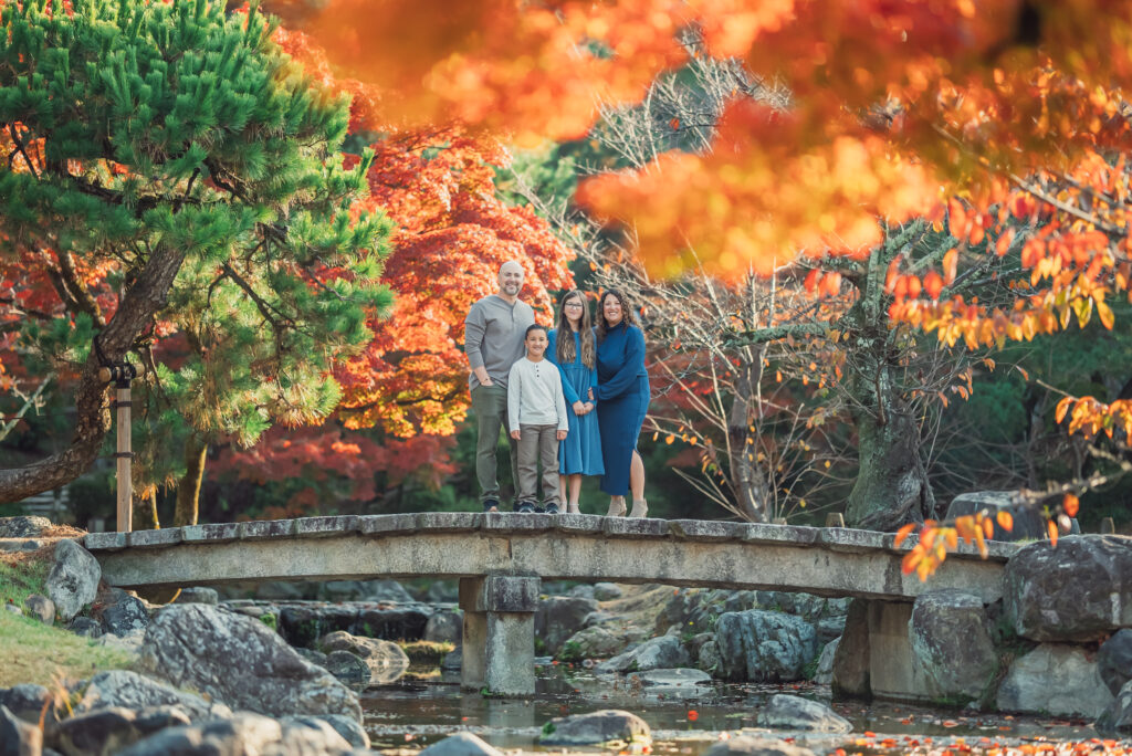 A family standing on a bridge surrounded by beautiful autumn leaves in Maruyama Park Kyoto during a family photoshoot