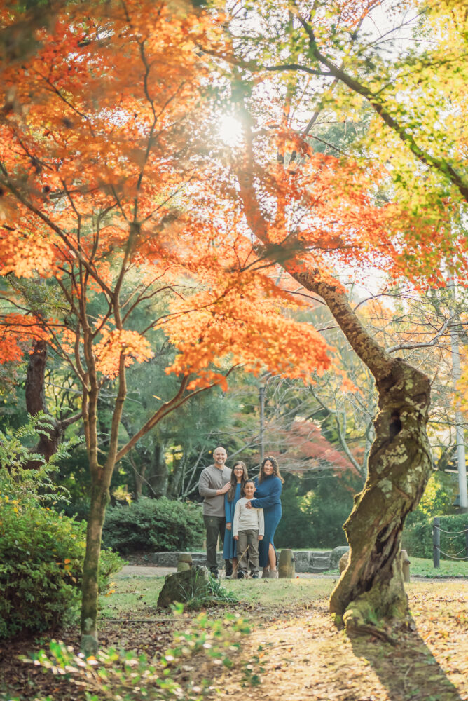 A family posing together with beautiful red autumn leaves at Maruyama Park during a Kyoto family photoshoot