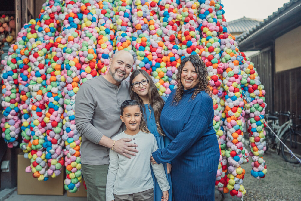 A family posing with the colorful kukurizaru wishing monkeys at Yasaka Koshindo Temple in Kyoto during a family photoshoot