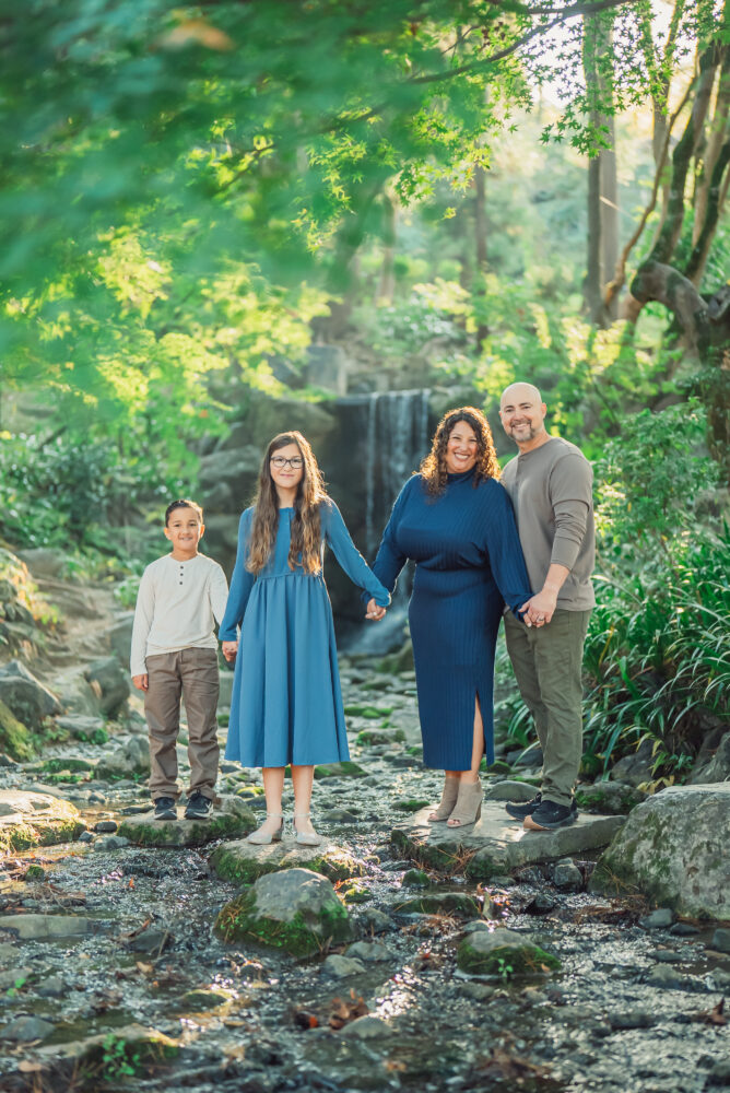 A family standing on stepping stones in front of a small waterfall at Maruyama Park during a Kyoto family photoshoot