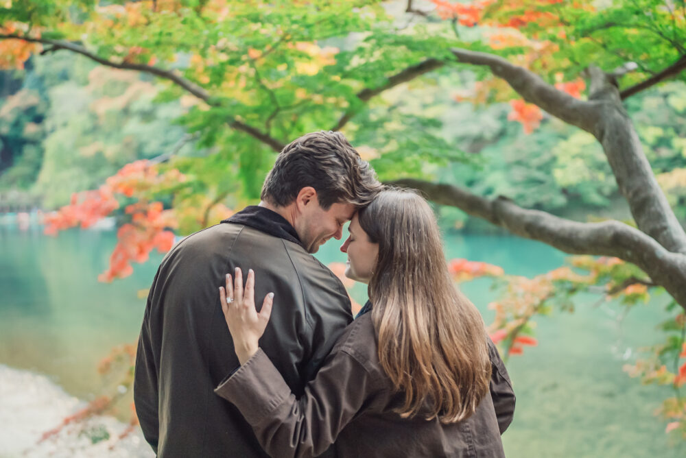 Romantic couple standing with Hozu River and colorful autumn leaves in Arashiyama Kyoto during a photoshoot