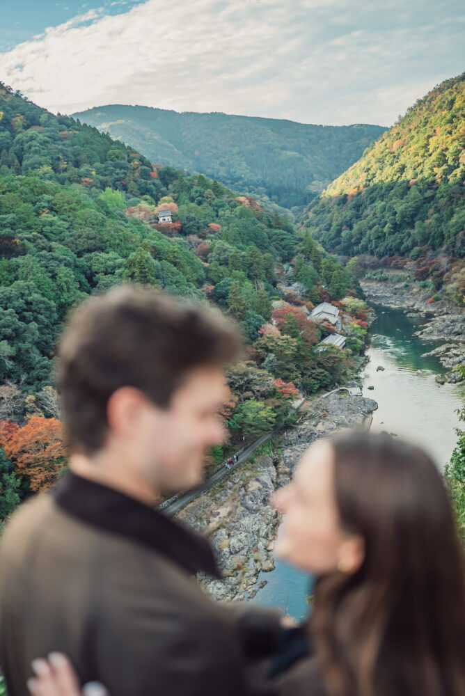 Couple standing at a viewpoint overlooking Hozu River and autumn mountains in Arashiyama Kyoto