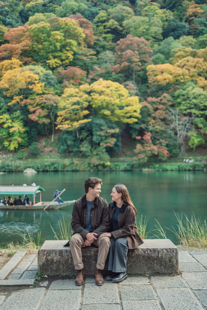 Couple standing together with a panoramic view of Hozu River, mountains, and autumn foliage in Kyoto
