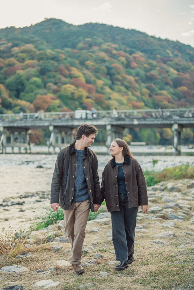 Couple celebrating their engagement with autumn mountains and Togetsukyo Bridge scenery in Arashiyama Kyoto