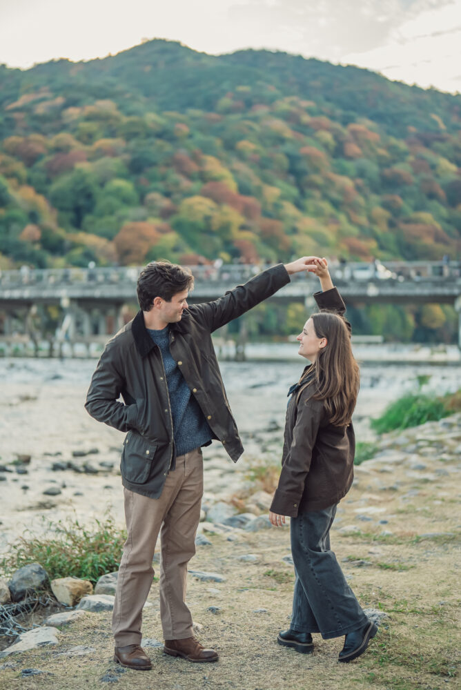 Couple standing together with a beautiful view of Togetsukyo Bridge, mountains, and nature in Arashiyama Kyoto
