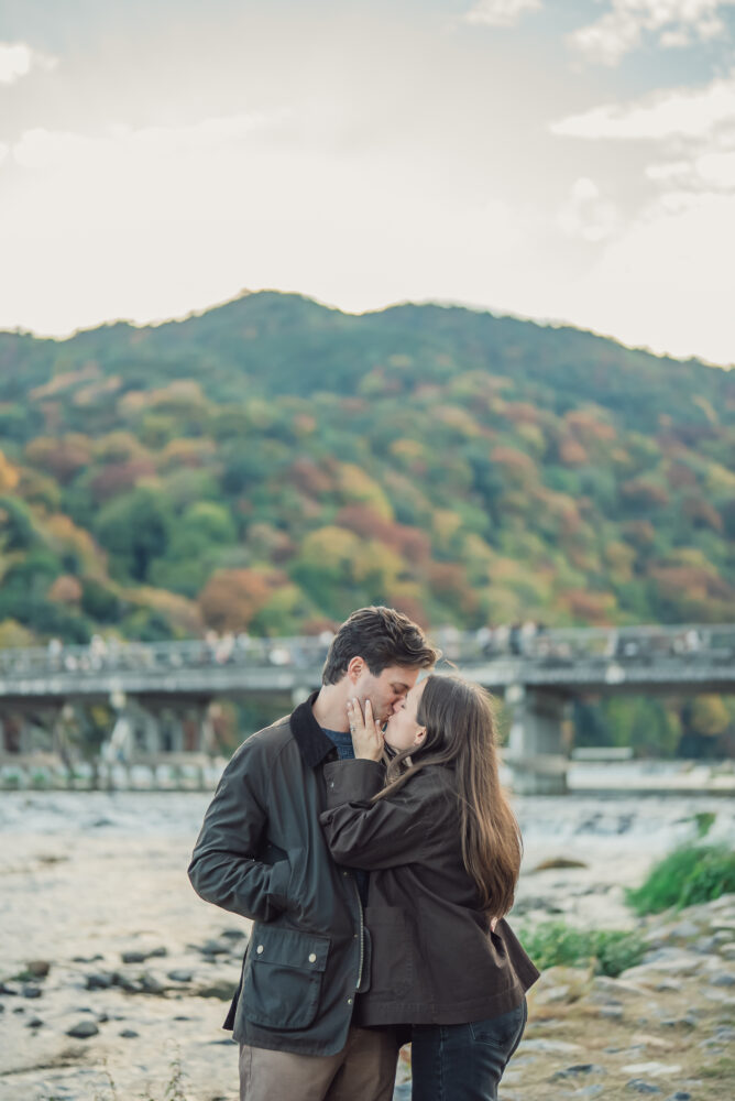 Engaged couple photographed with Togetsukyo Bridge and colorful autumn foliage in Arashiyama Kyoto during a proposal photoshoot
