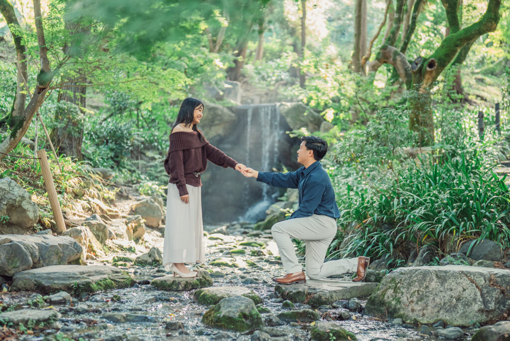 Couple celebrating a romantic proposal in front of a waterfall at Maruyama Park in Kyoto