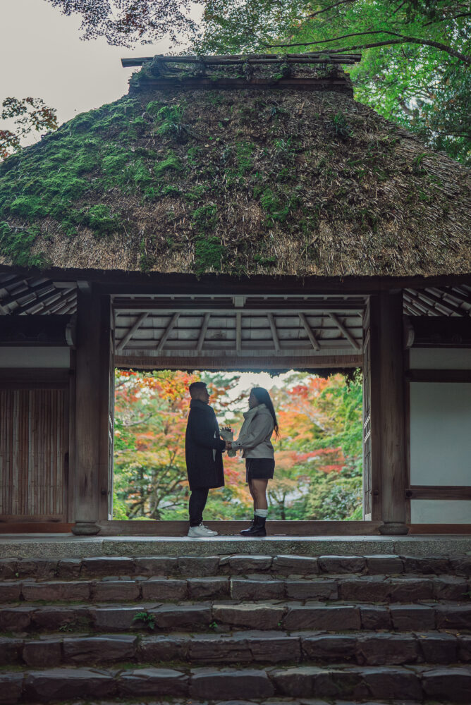 A romantic couple silhouette standing in front of a traditional Kyoto temple gate surrounded by beautiful autumn leaves