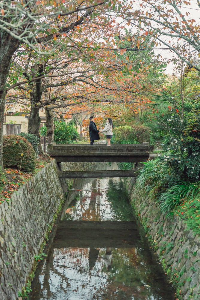 A couple enjoying beautiful autumn leaves while standing on a small bridge over the canal at Philosopher's Path Kyoto