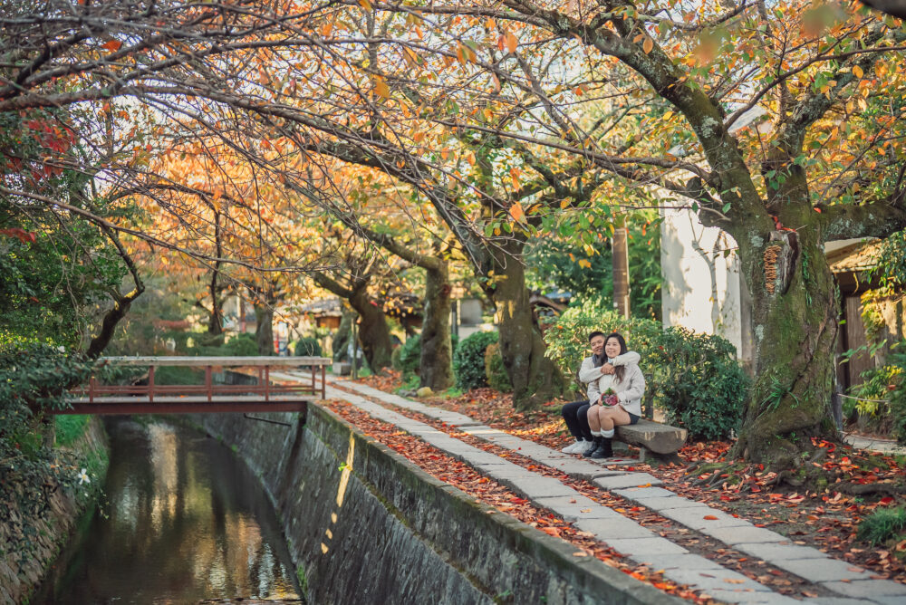 A romantic couple sitting on a bench at Philosopher's Path Kyoto enjoying the beautiful autumn leaves and peaceful seasonal scenery