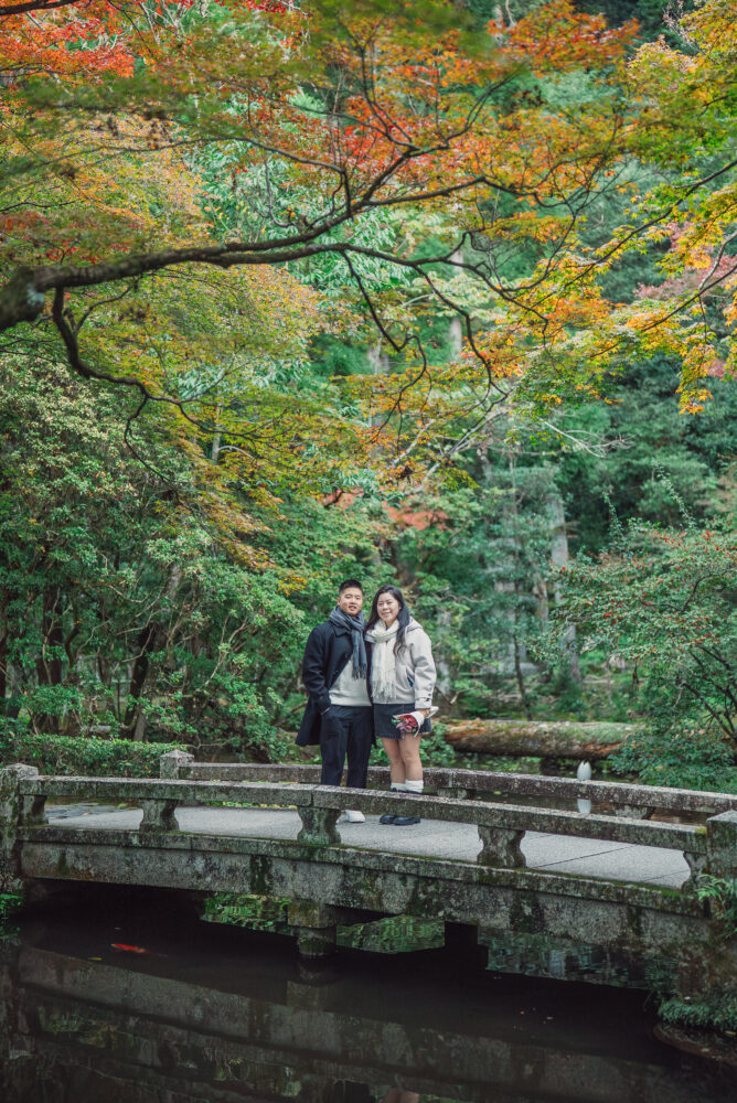 A romantic couple standing on a bridge in Kyoto surrounded by beautiful autumn leaves and colorful seasonal scenery