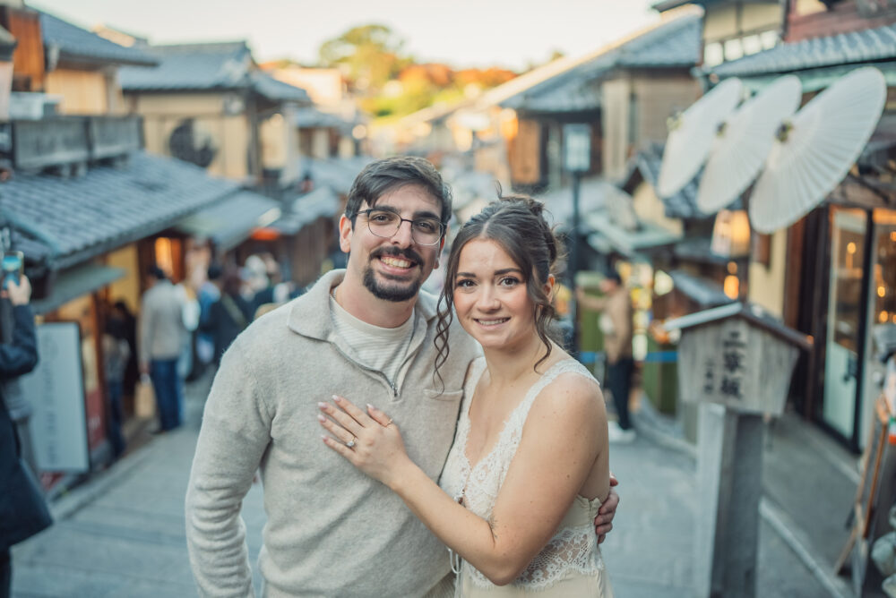 A romantic couple smiling together on Ninen-zaka street in Kyoto with traditional wooden buildings and historic scenery in the background