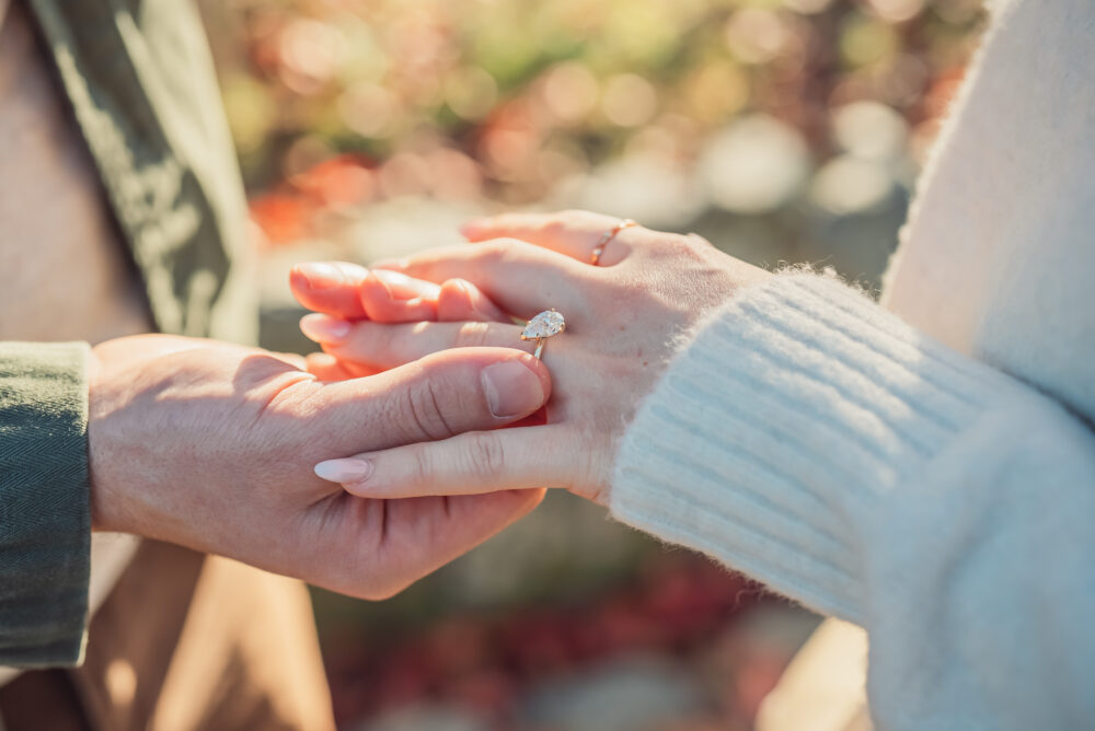 A romantic proposal moment in Kyoto where a man places an engagement ring on his partner's finger surrounded by autumn leaves and soft golden light