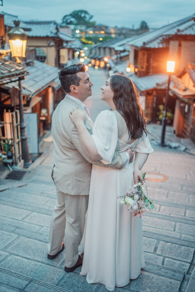 A romantic couple looking at each other on Ninen-zaka in Higashiyama Kyoto with traditional street lights during an early morning Kyoto elopement and pre wedding photoshoot.