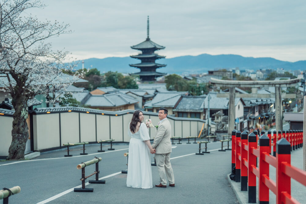A romantic couple looking back with Yasaka Pagoda and cherry blossoms in Higashiyama Kyoto during a spring Kyoto elopement and pre wedding photoshoot.