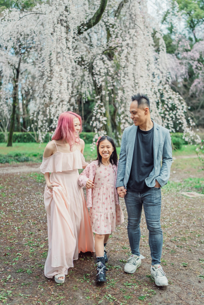 A family walking naturally near blooming weeping cherry trees at Kyoto Gyoen National Garden during a Kyoto spring photoshoot