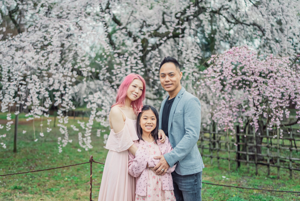 A family hugging naturally in front of early blooming weeping cherry blossoms at Kyoto Gyoen National Garden during a Kyoto spring photoshoot