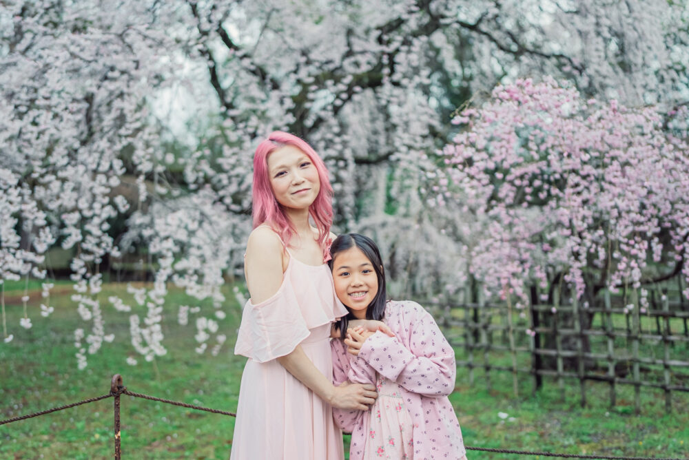 A mother and daughter hugging naturally in front of early spring weeping cherry blossoms during a Kyoto family photography session