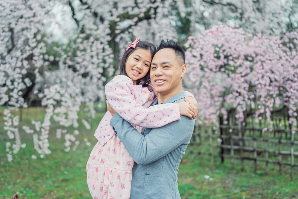 A father and daughter hugging naturally under blooming cherry trees during a Kyoto spring family photography session