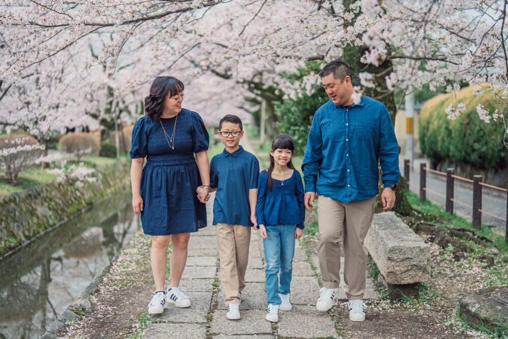 A family enjoying a natural photoshoot while walking under full bloom cherry blossoms along Philosopher’s Path in Kyoto during spring