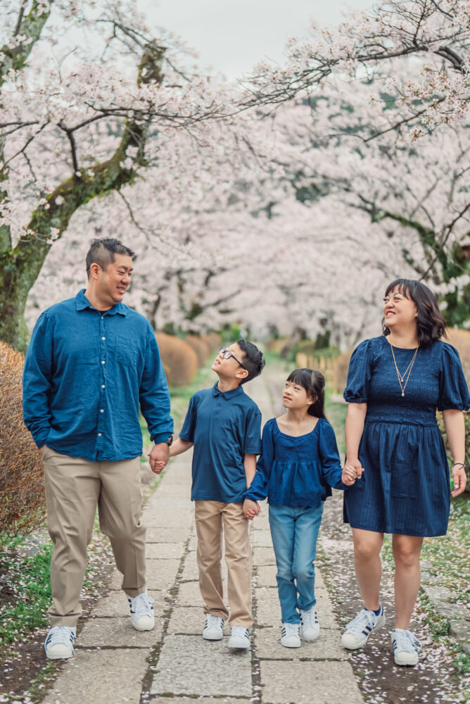 A happy family enjoying a natural Kyoto family photoshoot under a cherry blossom tunnel at Philosopher’s Path during spring