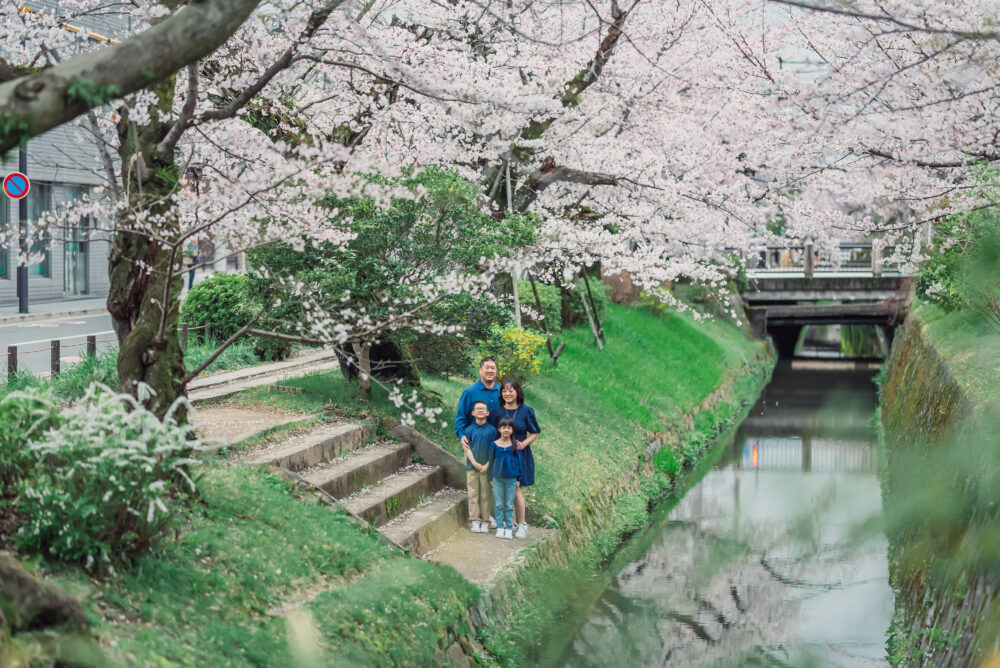 A family enjoying a natural Kyoto family photoshoot while viewing cherry blossoms beside the canal on Philosopher’s Path during spring