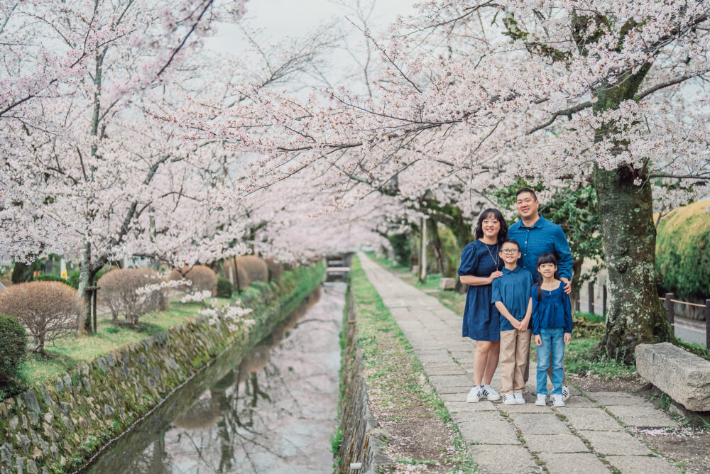 A smiling family standing by the canal under blooming cherry blossoms on Philosopher’s Path in Kyoto during spring