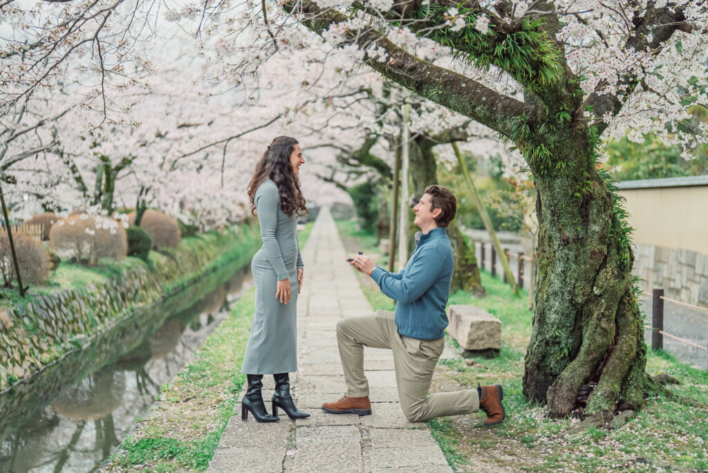 A surprise proposal beneath full-bloom cherry blossoms at Philosopher's Path in Kyoto during a spring morning photoshoot.