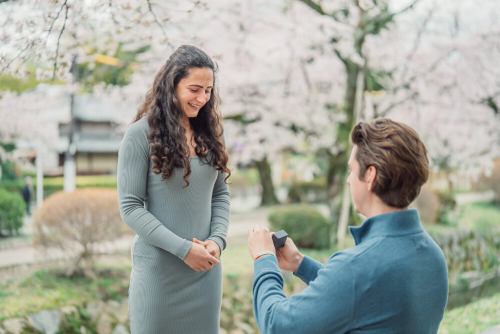 A woman smiling with joy after a surprise proposal beneath the cherry blossoms at Philosopher's Path in Kyoto.