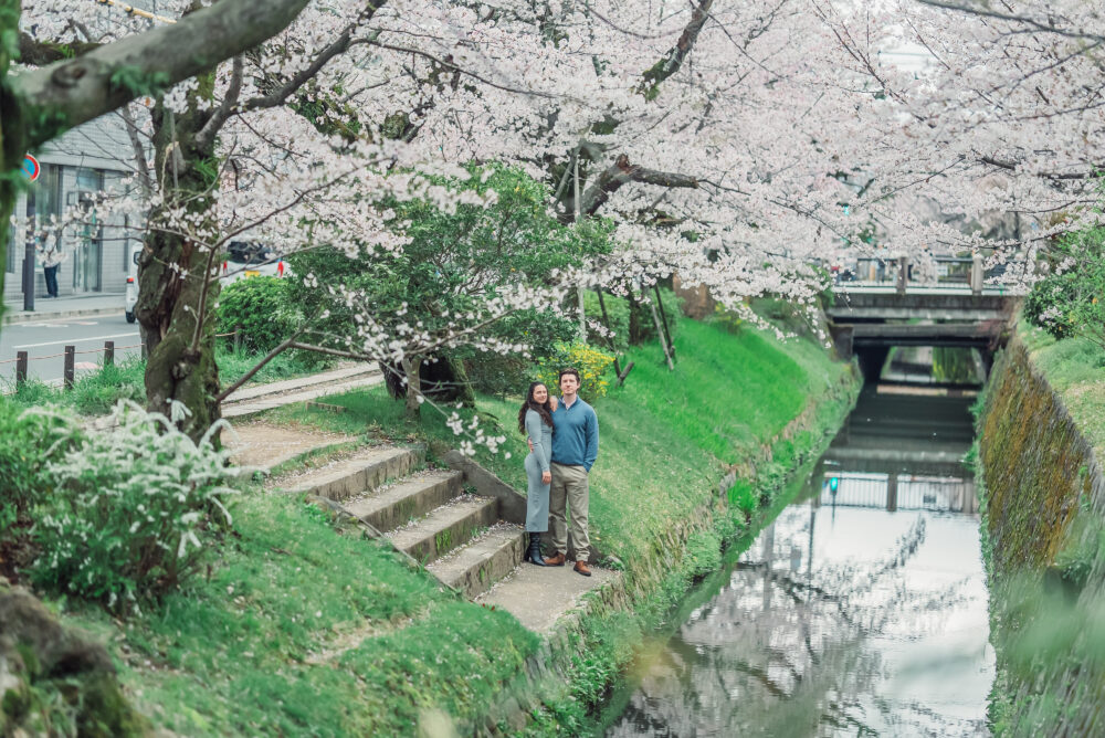 A couple standing together by a canal surrounded by blooming cherry blossoms on Philosopher’s Path in Kyoto