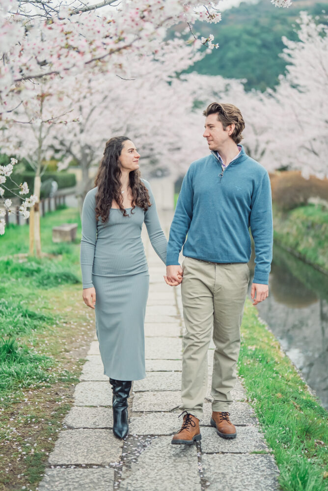 A couple walking hand in hand through a tunnel of blooming cherry blossoms along a canal on Philosopher’s Path in Kyoto