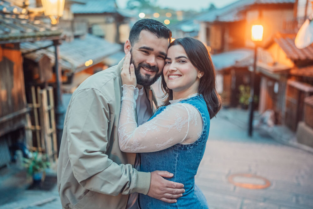 A happy couple smiling together with the traditional Ninen-zaka street in Higashiyama Kyoto in the background during an engagement photoshoot.