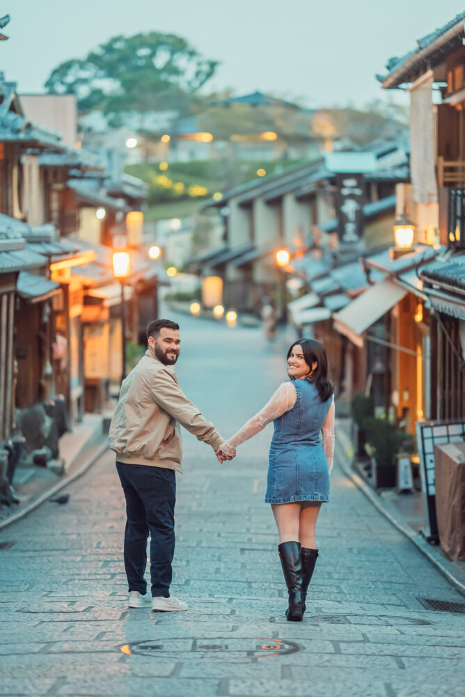 A couple walking together through the beautiful lantern-lit Ninen-zaka street in Higashiyama Kyoto during a romantic engagement photoshoot.