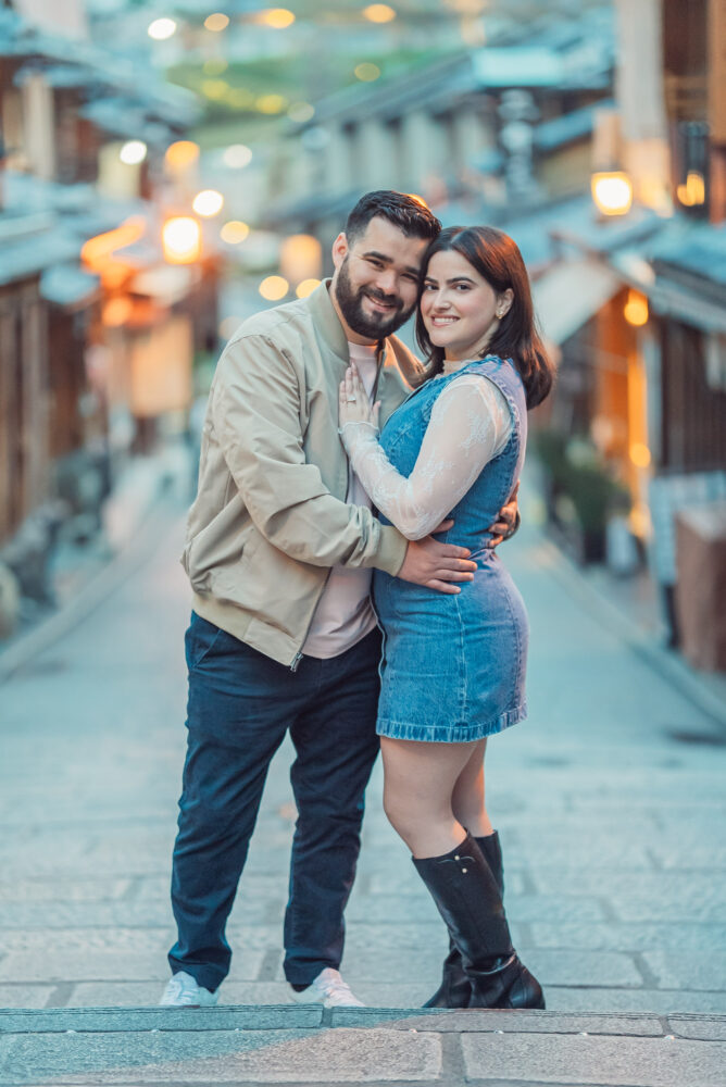 A romantic couple walking through Ninen-zaka in Higashiyama Kyoto with traditional street lights during a Kyoto engagement photoshoot.