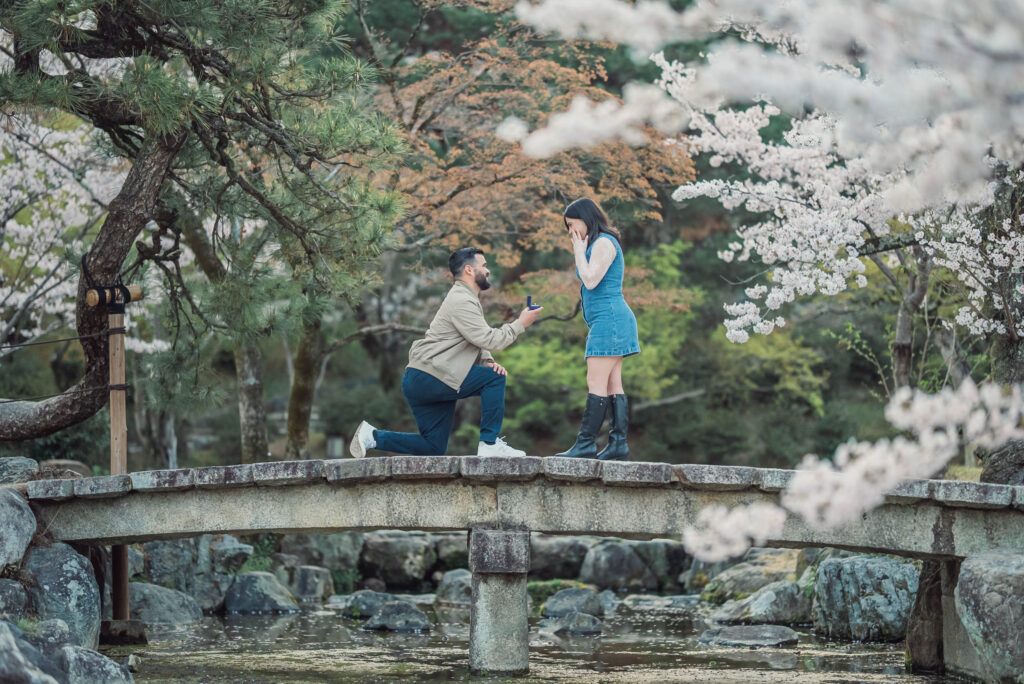A couple recreates their engagement proposal moment on a bridge at Maruyama Park in Kyoto with cherry blossoms during a spring sunrise photoshoot.
